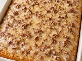Southern pecan praline sheet cake with butter pecan glaze in a white baking dish