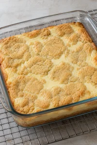 Lightly golden sugar cookie topping over baked cheesecake filling in a square glass dish