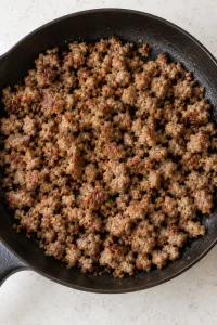 Cooked crumbled breakfast sausage in a skillet for the casserole