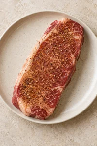 An uncooked strip steak lightly coated with the seasoning blend.