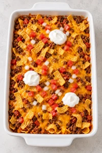 Walking taco casserole viewed from above with fresh tomato and sour cream toppings