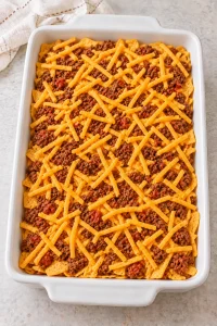 Walking taco casserole assembled in two layers with shredded cheddar before baking